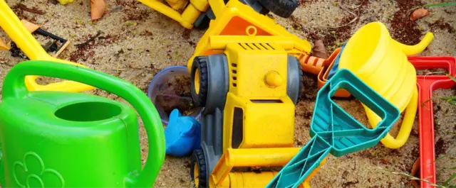 Plastikspielzeug in einer Sandkiste. Bagger, Schaufel, grüne Gieskanne liegen durcheinander.